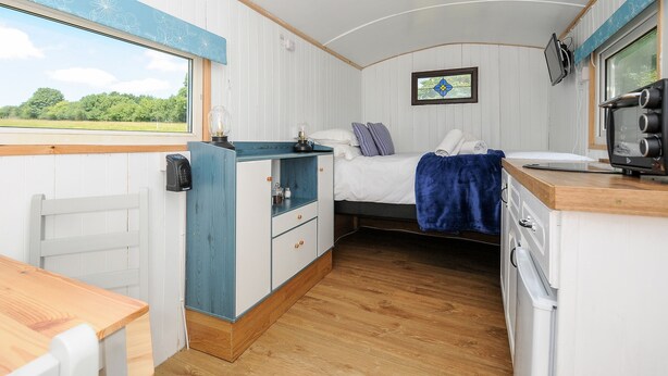 Habitación compacta y bien iluminada con cama, una mesita, kitchenette y ventana con vistas a zonas verdes.