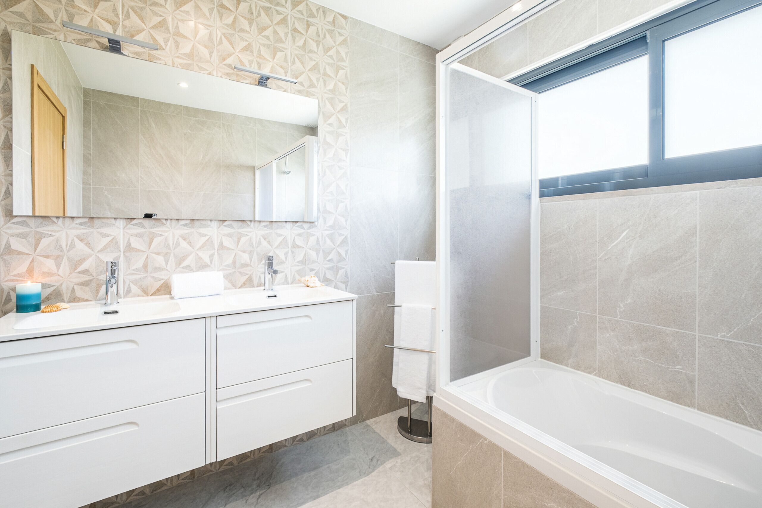 Une salle de bain moderne avec un grand miroir, un lavabo avec un robinet, un porte-serviettes et un espace douche.