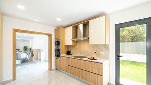 A modern kitchen with wooden cabinets, a stainless steel sink, and a view of the backyard through a sliding glass door. - Family villa with heatable pool and BBQ (Albufeira)