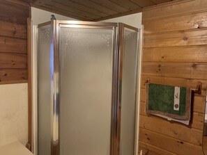 Un baño con cabina de ducha de vidrio, paredes de madera y una toalla colgada en un perchero.