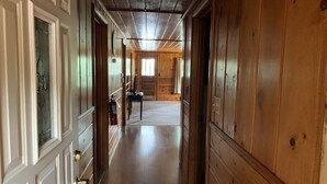 A long, narrow hallway with wooden walls and doors, leading to a room with a window and a table. - Gresham Shores - Hungry Bear - PET FRIENDLY (Arbor Vitae)