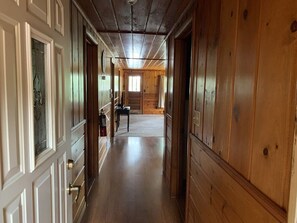 Ein langer, schmaler Flur mit Holzwänden und -türen, der zu einem Zimmer mit Fenster und Tisch führt.