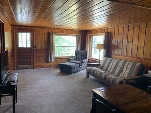 Interior acogedor de una cabaña con paredes de madera, un sofá, una silla y una mesita.