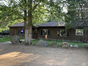 Une cabane en bois à deux étages, dotée d’un porche à l’avant, de grandes fenêtres et d’une porte de garage bien visible.