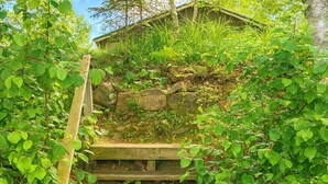 Un escalier en bois, entouré d’une végétation luxuriante, mène à un bâtiment doté d’un toit en pente.