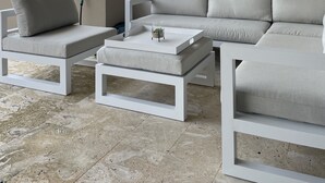 A modern outdoor seating area with a white sofa, two armchairs, and a coffee table, featuring a decorative wall piece and a view of the landscape. - Blue Bay Green View (Sint Michiel)