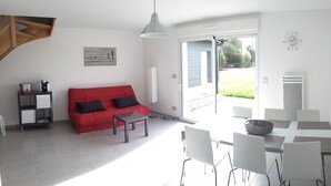 Un salon moderne avec un canapé rouge, une table basse et un coin repas comprenant une table et des chaises blanches.