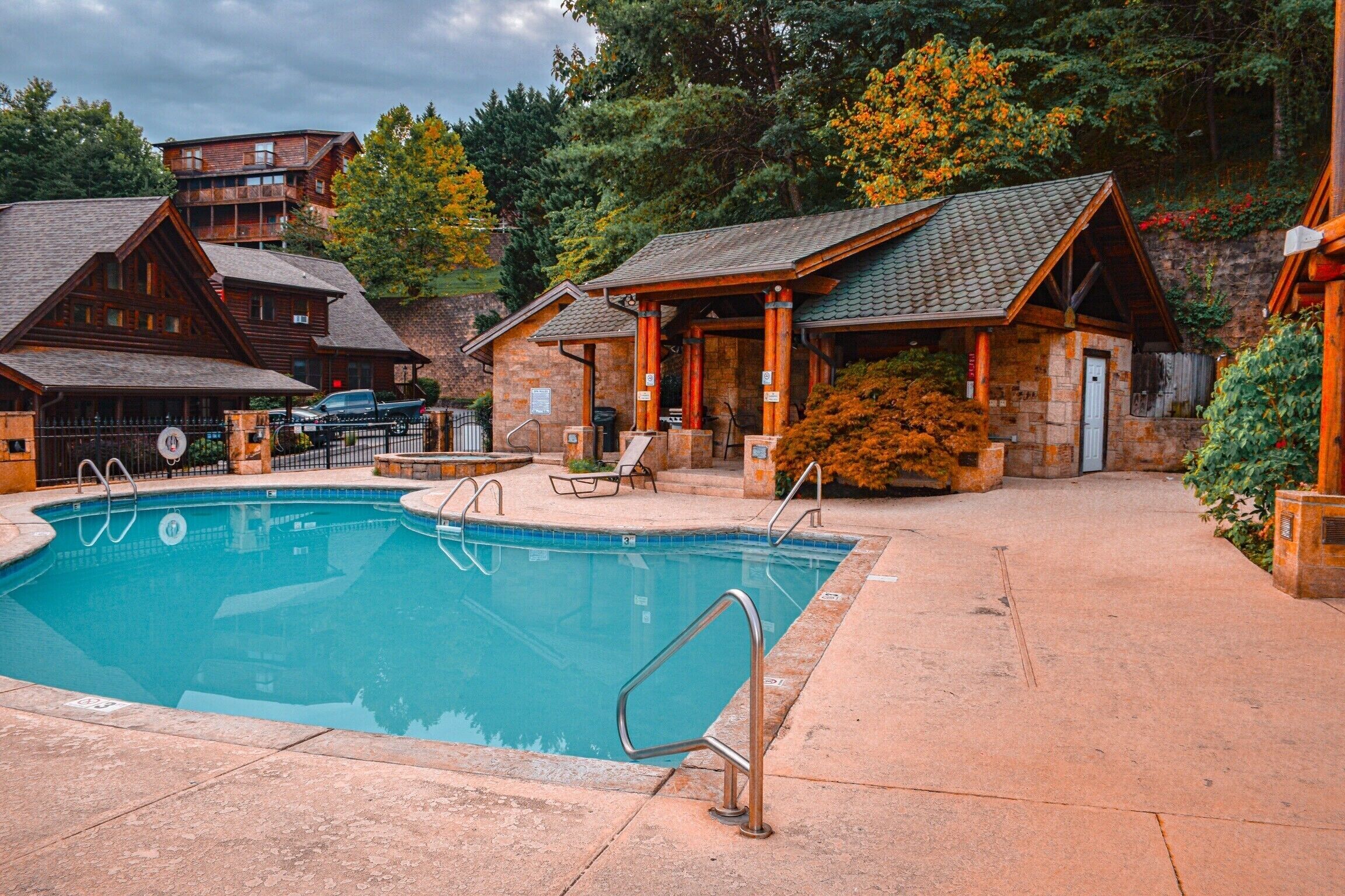 A pool area with a clear view of the pool, lounge chairs, and a building with a stone facade.