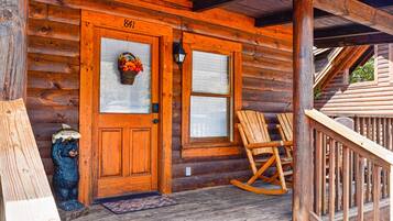 A wooden cabin with a double door, a welcome bear statue, a rocking chair, and a porch with a railing.