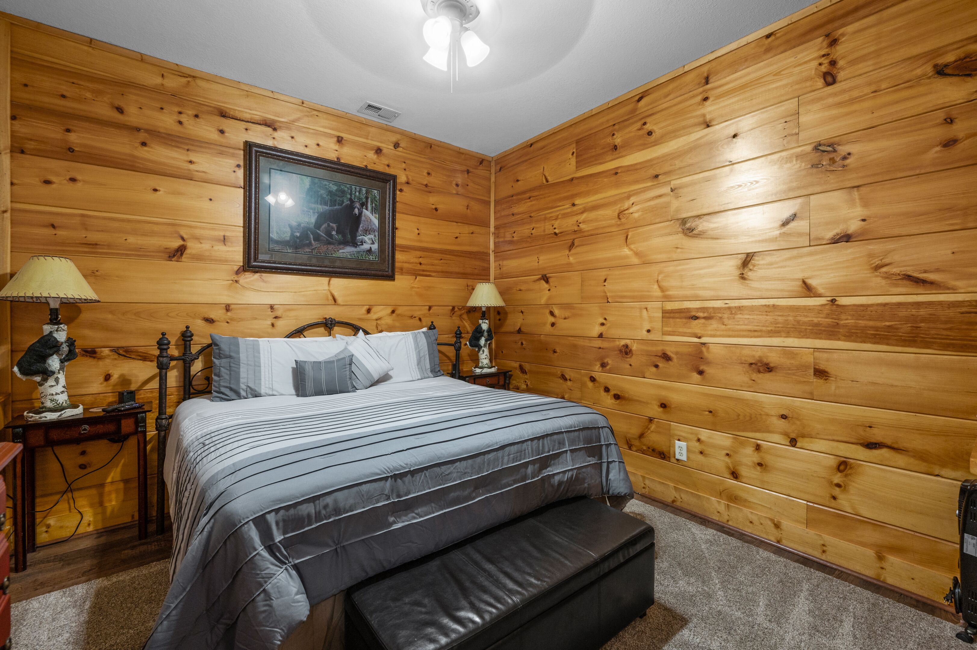 Ein Schlafzimmer mit Holzvertäfelung, einem Bett mit grauer Bettwäsche, zwei Nachttischen mit Lampen und einem gerahmten Bild an der Wand.