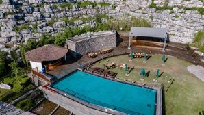 A swimming pool with a stone deck, a covered seating area, and a building with a thatched roof. - Blossom Hill Hotel Ya'an Mengdingshan (Ya'an)