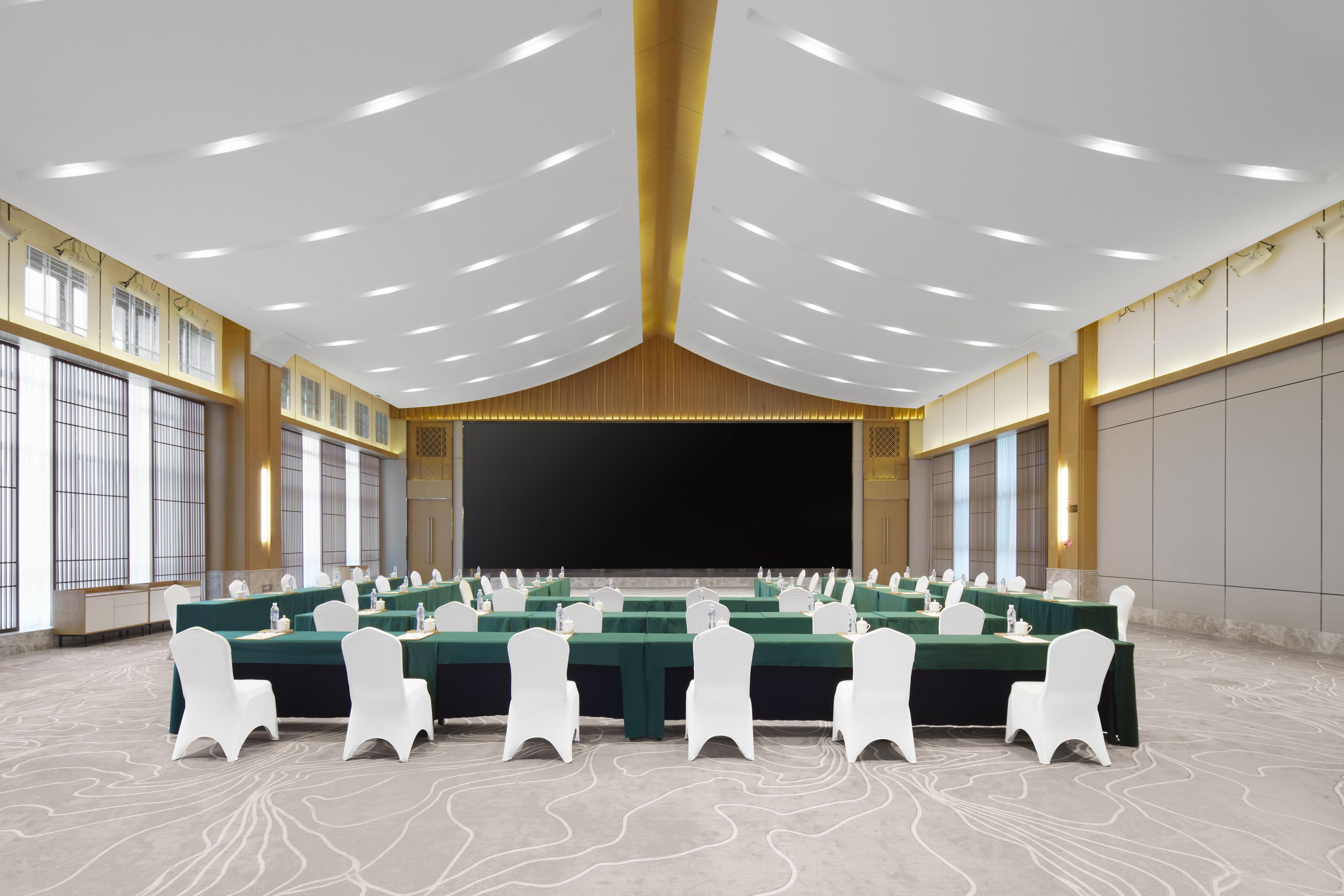 Un salón de conferencias con varias mesas, sillas blancas y una pantalla grande al frente.