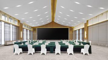 Un salón de conferencias con varias mesas, sillas blancas y una pantalla grande al frente.
