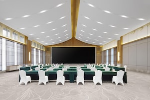 A conference room with multiple tables, white chairs, and a large screen at the front.