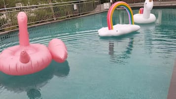 Una piscina con juguetes inflables, vistas a montañas y un edificio al fondo.