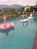 Una piscina con juguetes inflables, vistas a montañas y un edificio al fondo.