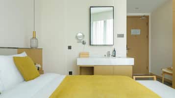 A hotel room with a bed, a bedside table with a lamp, a mirror, a wooden door, and a bathroom with a sink and mirror.