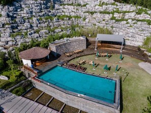 A swimming pool with a stone deck, a covered seating area, and a building with a thatched roof. - Blossom Hill Hotel Ya'an Mengdingshan (Ya'an)