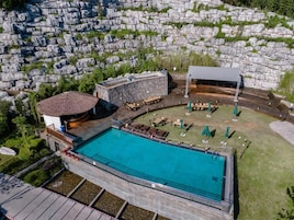A swimming pool with a stone deck, a covered seating area, and a building with a thatched roof.