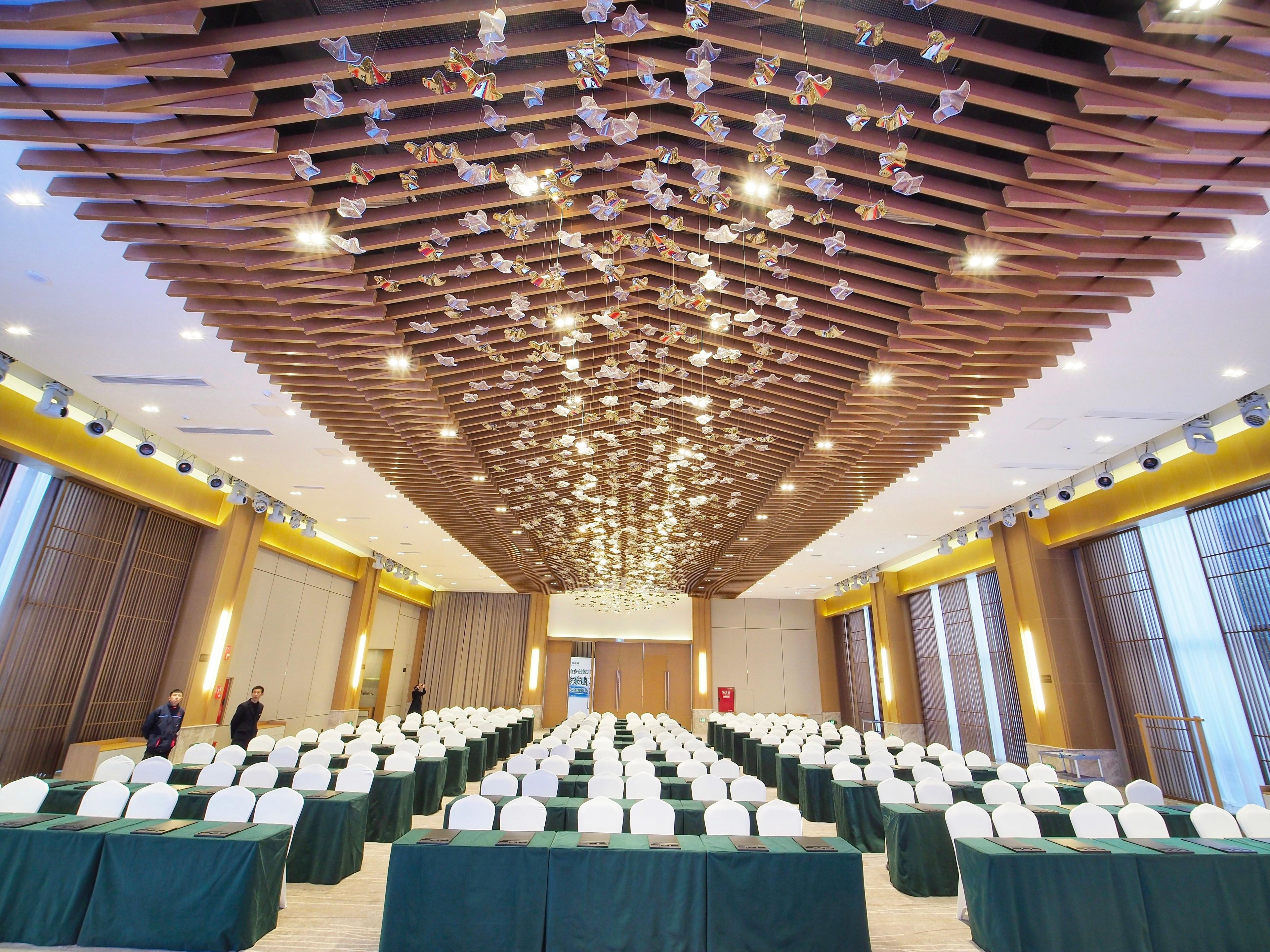 Un salón de conferencias con mesas dispuestas en filas, sillas blancas y un techo con adornos colgantes.
