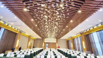 Un salón de conferencias con mesas dispuestas en filas, sillas blancas y un techo con adornos colgantes.