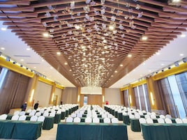 Un salón de conferencias con mesas dispuestas en filas, sillas blancas y un techo con adornos colgantes.