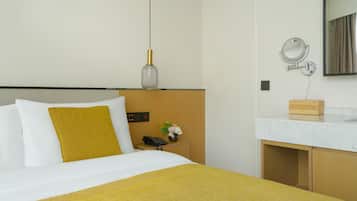 Una habitación de hotel con cama, mesita de noche, lámpara, espejo y un pequeño armario de madera.