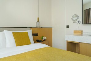 A hotel room with a bed, bedside table, lamp, mirror, and a small wooden cabinet. - Blossom Hill Hotel Ya'an Mengdingshan (Ya'an)