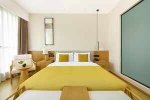 Habitación de hotel con una cama grande, una mesita de noche con lámpara, una silla y un ventanal amplio.
