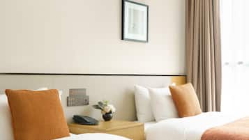 A hotel room with two beds, a nightstand with a phone, a vase with flowers, and a window with curtains.