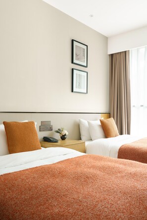 A hotel room with two beds, a nightstand with a phone, a vase with flowers, and a window with curtains.