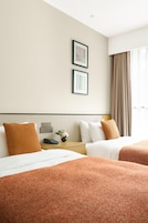 A hotel room with two beds, a nightstand with a phone, a vase with flowers, and a window with curtains.