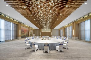 A large conference room with a round table surrounded by white chairs with blue sashes, a wooden ceiling with hanging lights, and large windows on the sides. - Blossom Hill Hotel Ya'an Mengdingshan (Ya'an)