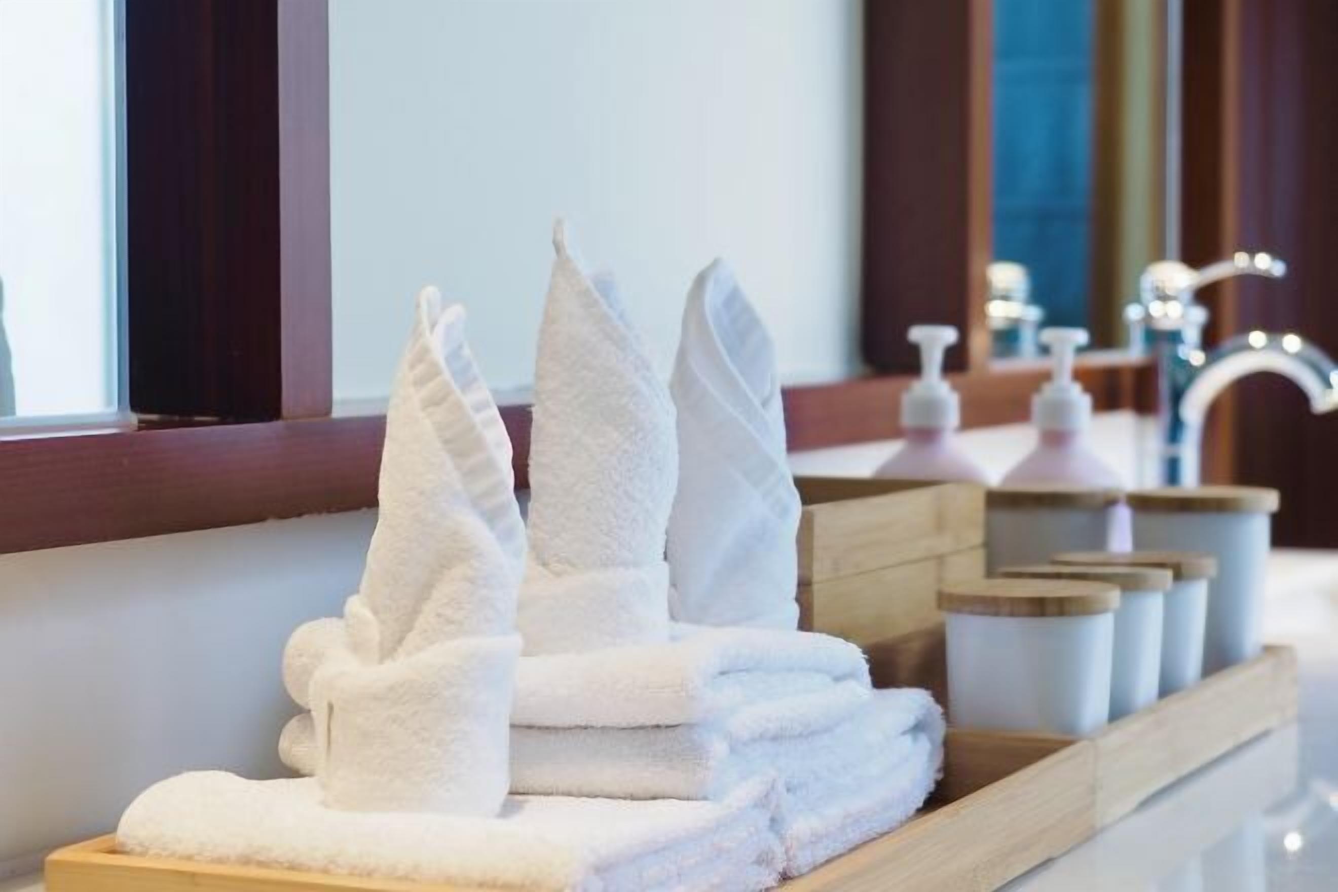 Un montón ordenado de toallas blancas sobre una bandeja de madera en un baño de hotel.