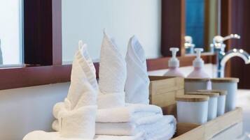 Un montón ordenado de toallas blancas sobre una bandeja de madera en un baño de hotel.