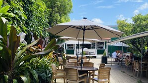 An outdoor patio with wooden tables and chairs, surrounded by lush greenery. - Fresh, Bright, Cute. Near Hanalei! Walk to the ocean in minutes. (Princeville)