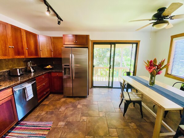 A kitchen with wooden cabinets, a stainless steel refrigerator, a dining table with chairs, and a view of the outdoors through a sliding glass door.