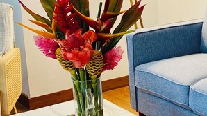 A room with a white table, a vase of flowers, a blue couch, and a lamp. - Fresh, Bright, Cute. Near Hanalei! Walk to the ocean in minutes. (Princeville)