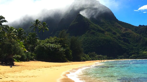 A beach with clear turquoise waters, a sandy shore, and a mountain with clouds in the background. - Fresh, Bright, Cute. Near Hanalei! Walk to the ocean in minutes. (Princeville)