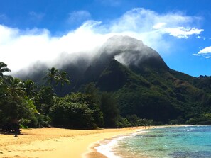 Een strand met helder turquoise water, een zandstrand en een berg met wolken op de achtergrond.