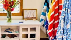 A room with a white desk, a vase with flowers, a framed painting, and colorful towels hanging on a rack. - Fresh, Bright, Cute. Near Hanalei! Walk to the ocean in minutes. (Princeville)