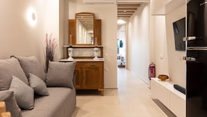 A modern living room with a sofa, a wooden cabinet, and a large mirror. - Modernly furnished family suite with sea view, just in front of the Palm beach (Rethymno)