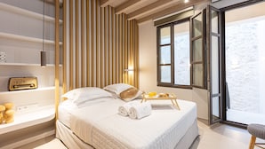 A modern hotel room with a large bed, a bedside table with a radio, a tray with breakfast items, and a view of the outdoors through a large window. - Modernly furnished family suite with sea view, just in front of the Palm beach (Rethymno)