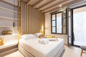 Habitación de hotel moderna con una cama grande, una mesita de noche con una radio, una bandeja con artículos de desayuno y vistas al exterior a través de un ventanal amplio.