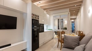 A modern kitchen with white cabinets, a black refrigerator, and a dining area with a wooden table and chairs. - Modernly furnished family suite with sea view, just in front of the Palm beach (Rethymno)