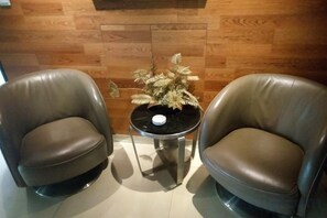Two leather armchairs, a small round table with a decorative plant, and a wooden wall.