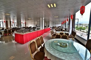 Un vaste espace dédié à la salle à manger, avec des tables et des chaises rondes, un buffet central et de grandes fenêtres offrant une vue panoramique.