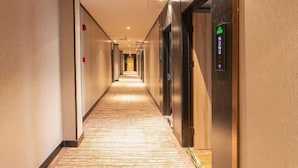 Un pasillo de hotel con piso alfombrado, puertas a la derecha y un ascensor al final del pasillo.