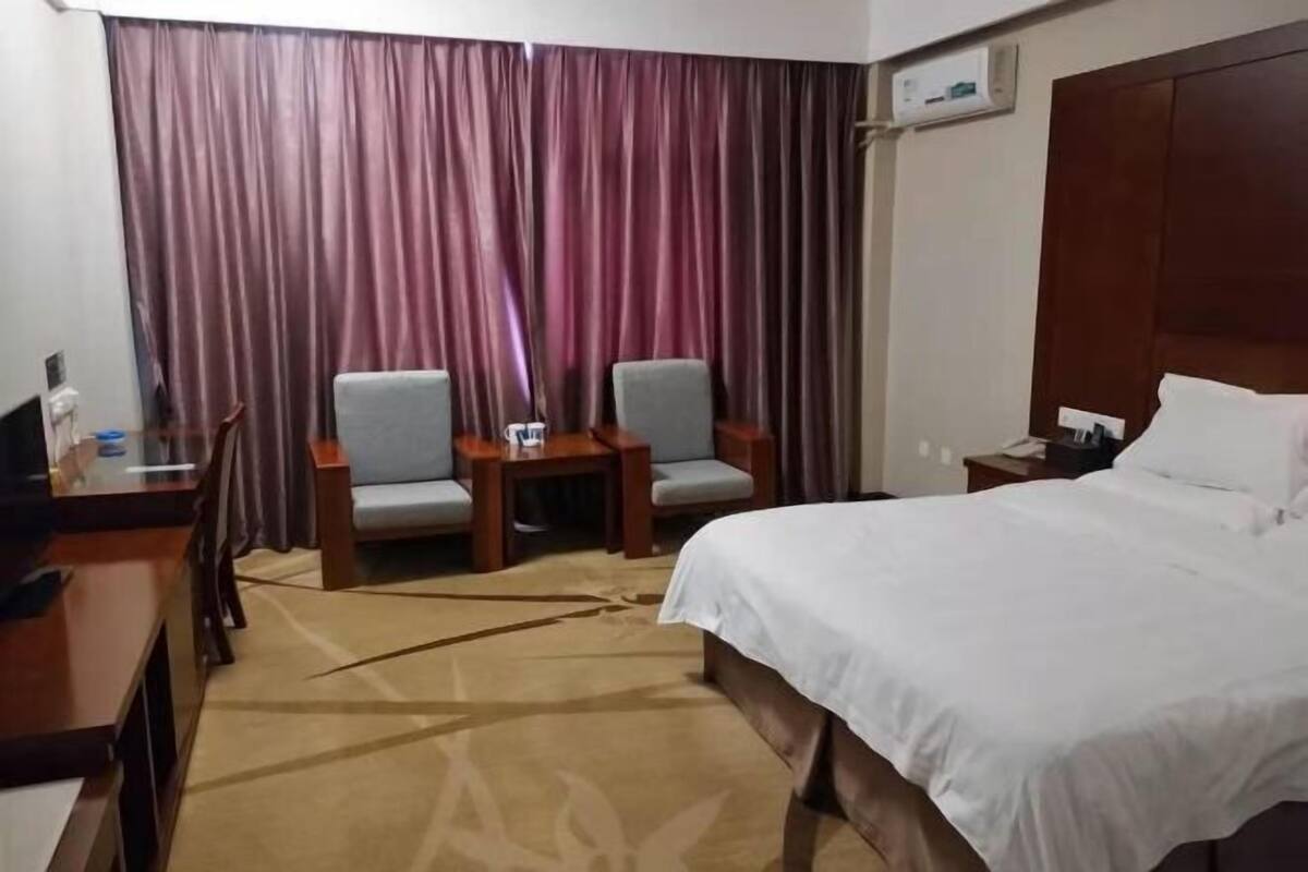 A hotel room with a bed, two chairs, a desk, and a curtain.