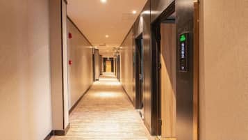 A hotel corridor with a carpeted floor, doors on both sides, and an elevator on the right.